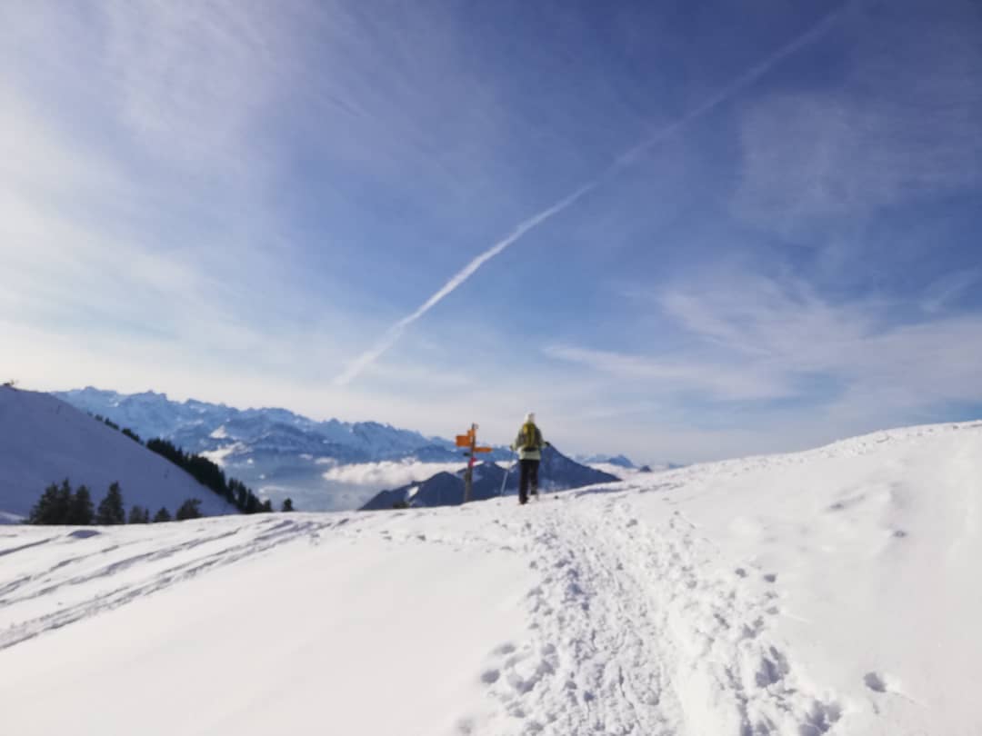 Hiker following a snowy mountain trail under a blue sky